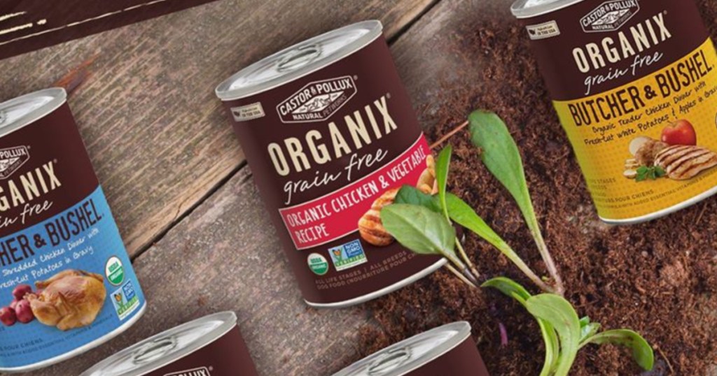 organix cans of dog food on wood surface with plants and dirt surrounding