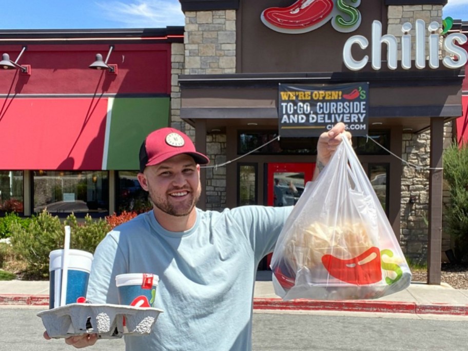 man holding up bag of food and drinks in front of restaurant