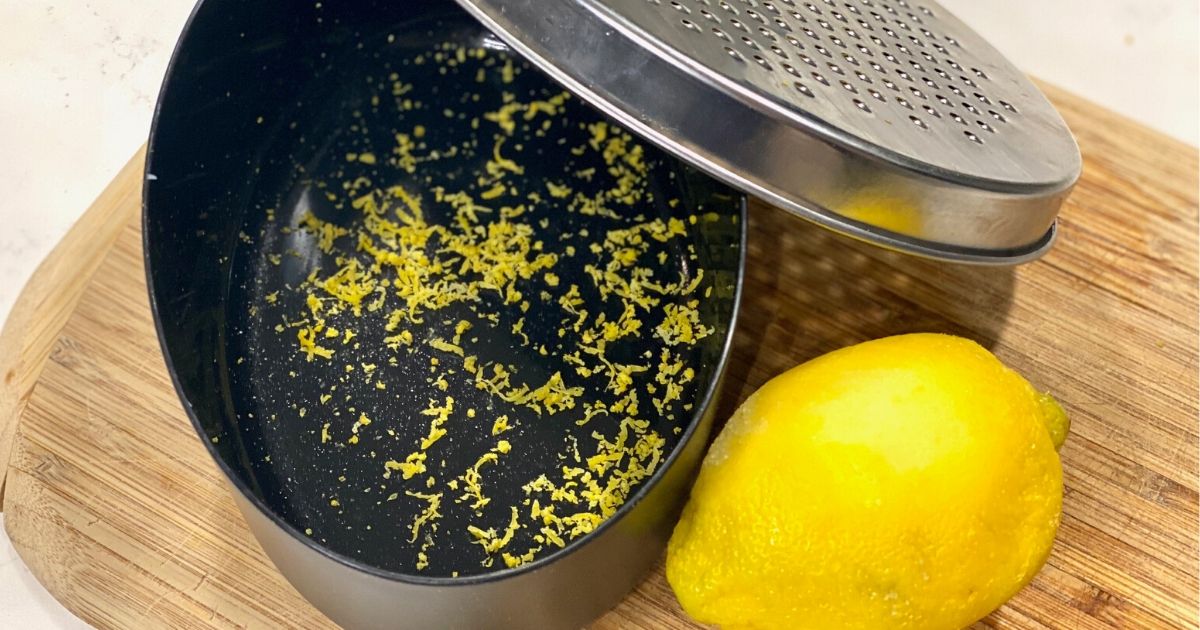 Lemon zest in cheese grater storage compartment next to a lemon