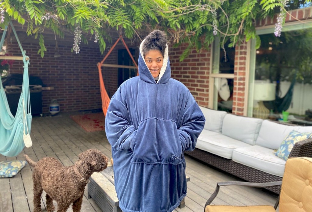 girl wearing an oversized blue wearable blanket outside on deck with dog
