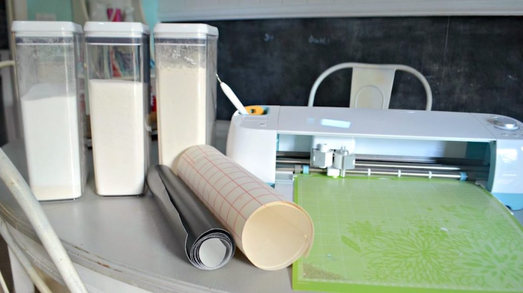 containers with dry baking food and rolls of adhesive sticker sitting next to cricut maching