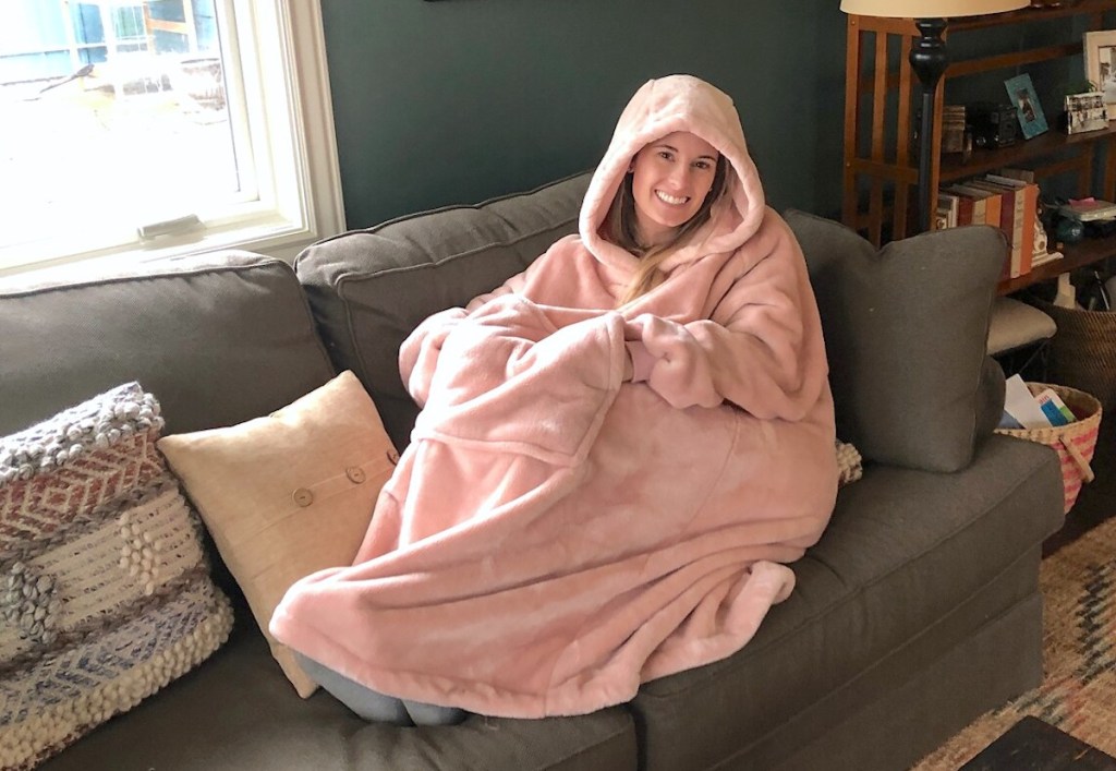 woman sitting on couch wearing oversized pink blanket