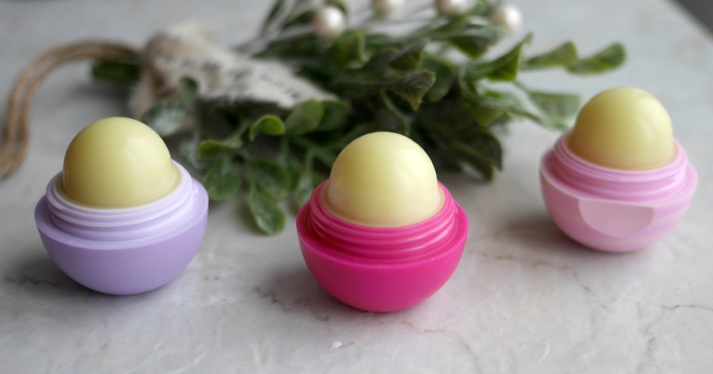 one purple, one bright pink, and one light pink open lip balms on counter with flower behind them