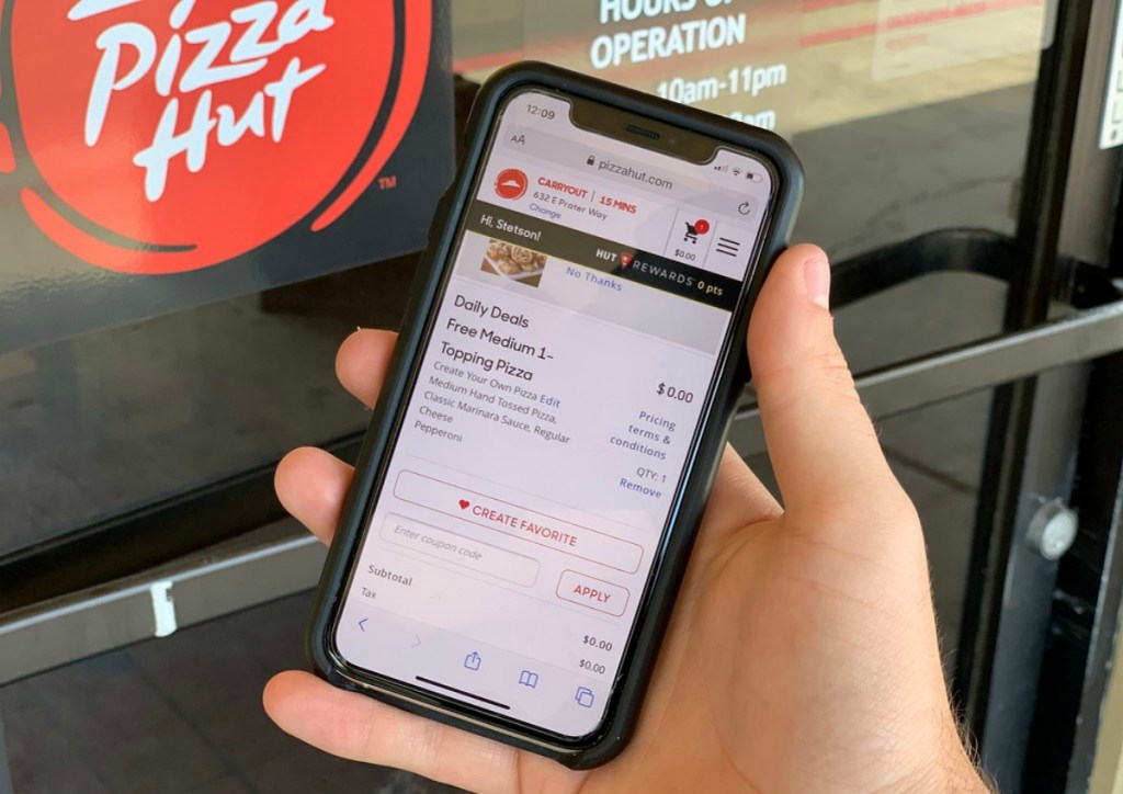 hand holding cell phone in front of pizza hut sign
