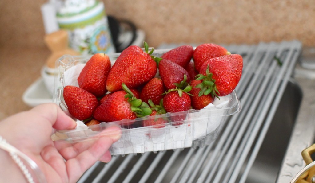 hand holding a clear container of fresh strawberries with paper towel on bottom