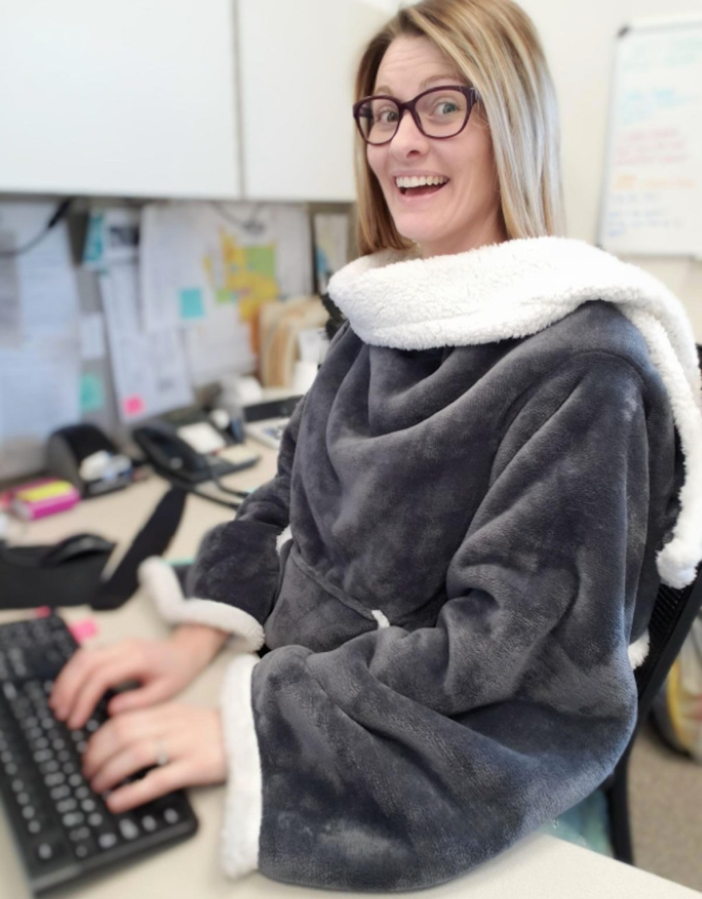 woman sitting at a desk wearing a dark gray blanket