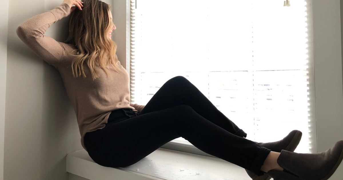 woman sitting looking out the window wearing brown sweater and black jeans
