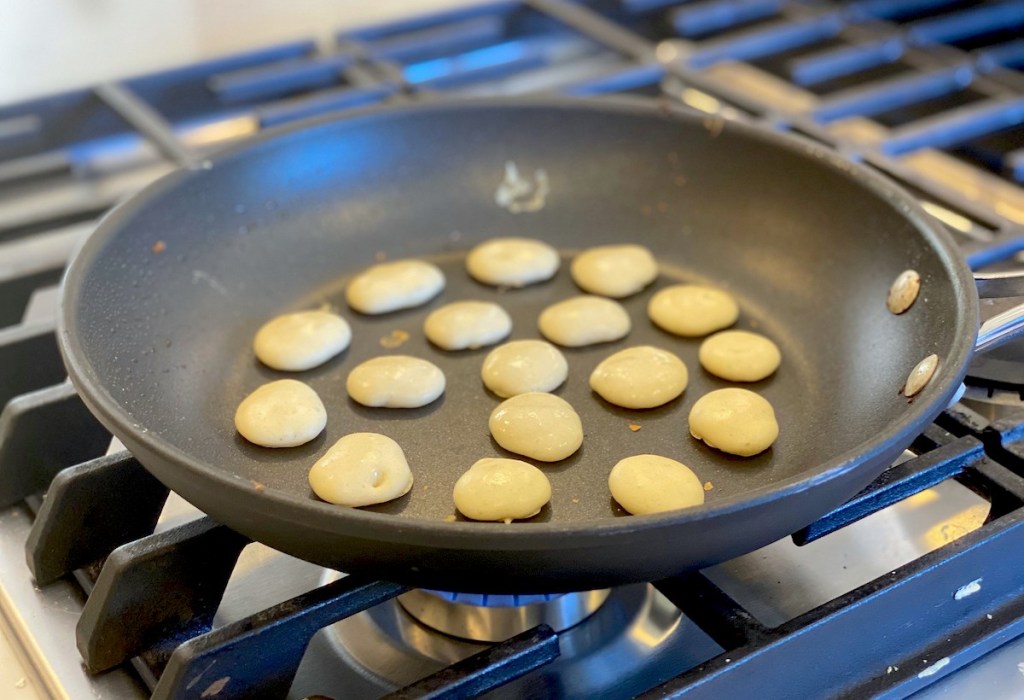 black pan with mini pancakes cooking on gas stove top
