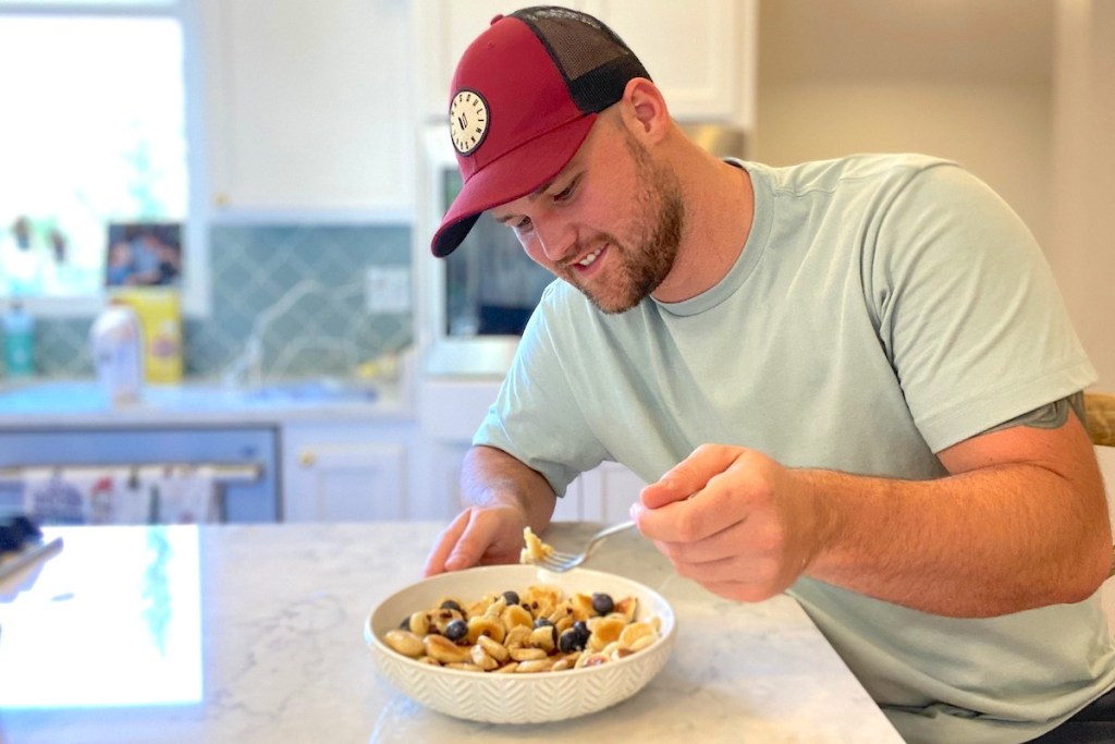 Man smiling and eating mini pancakes in bowl with a fork