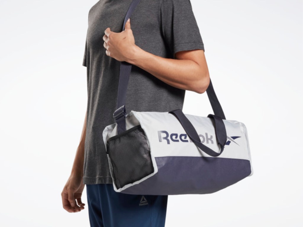 man wearing gray shirt carrying Reebok duffel bag