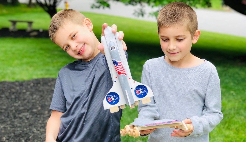 two boys holding wood rocket ship pieces smiling