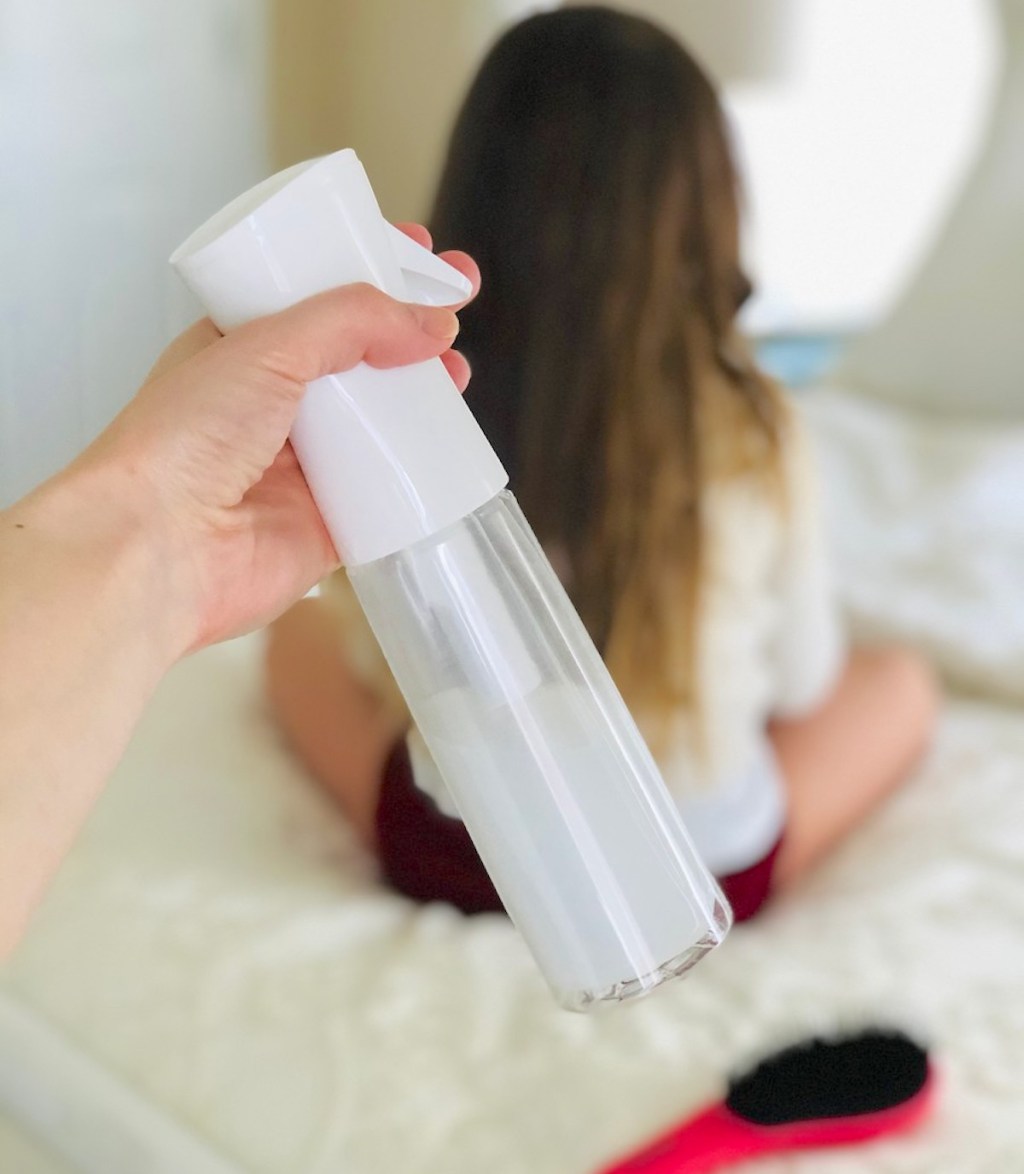 hand holding a spray bottle with kid sitting on bed