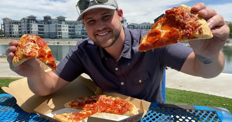 man sitting at picnic table holding up pizza slices