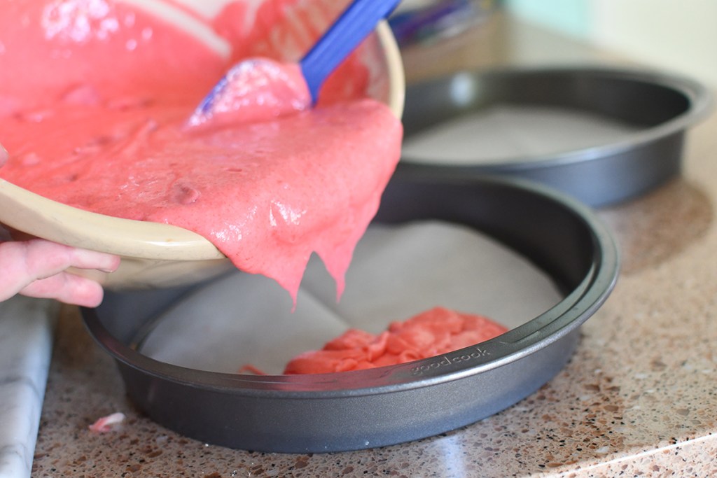 pouring strawberry cake batter into cake pan