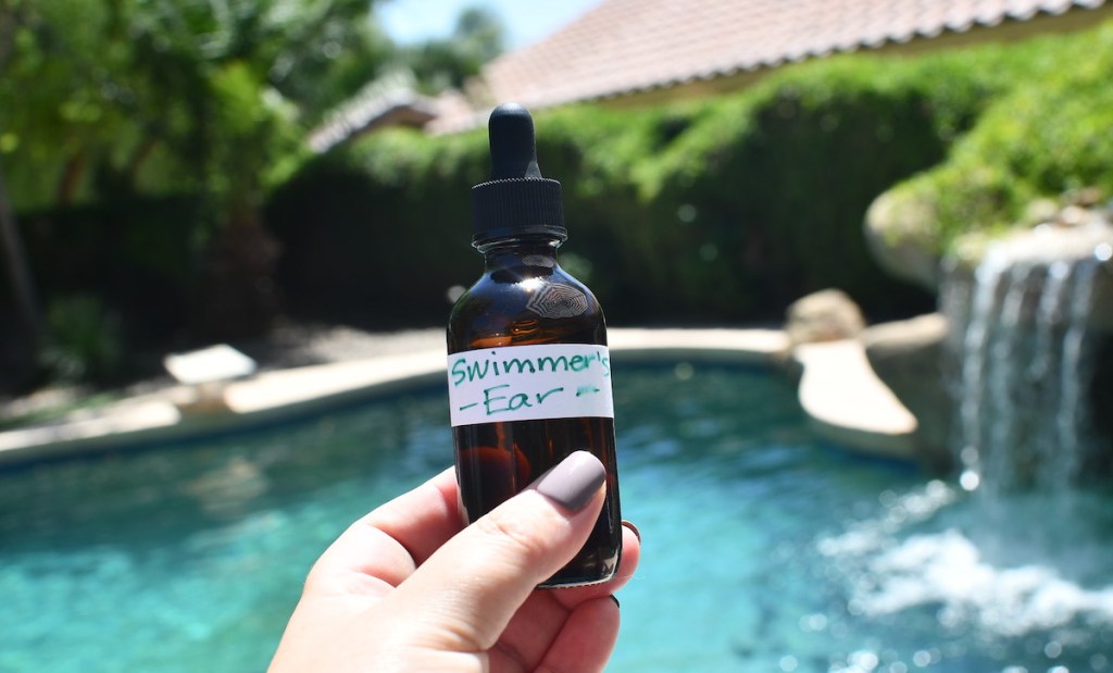 hand holding an amber dropper bottle in front of pool