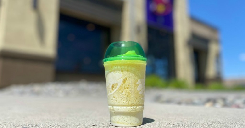 frozen pineapple drink in a cup on the ground in front of Taco Bell