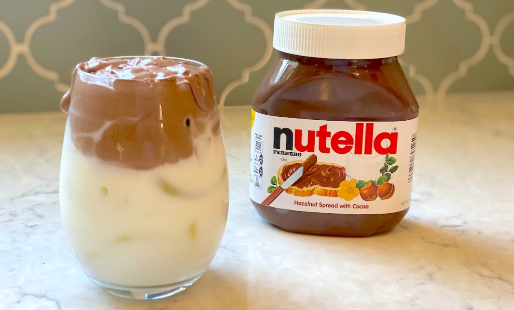 glass with half milk and nutella sitting on countertop with jar of nutella