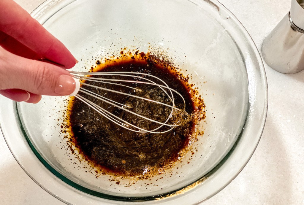 hand holding a whisk in clear bowl with brown liquid