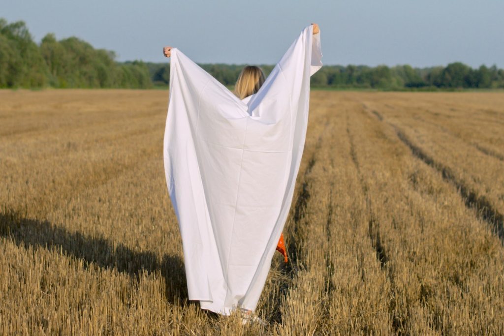 woman walking through field holding up white sheet