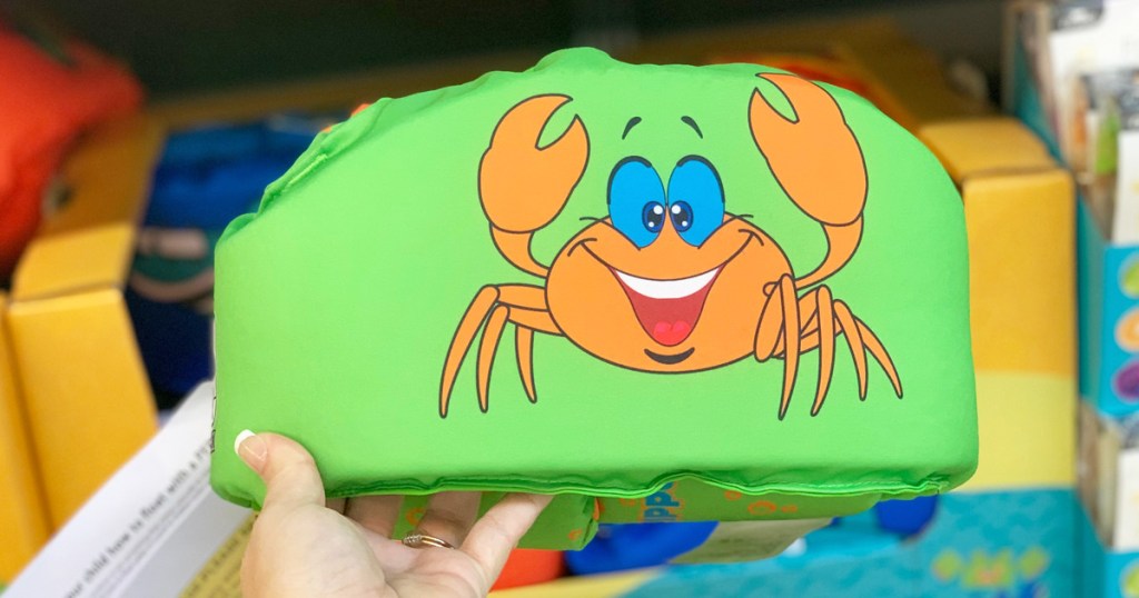 person holding a green kids life jacket vest with a crab printed on it