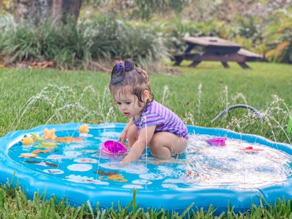 little girl squatting and playing in a blue colored splad pad with water flowing