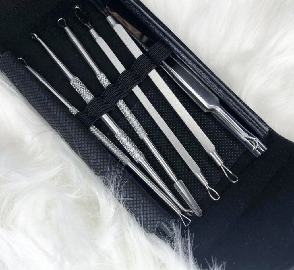 six silver blackhead removing tools inside a black case on white fuzzy blanket