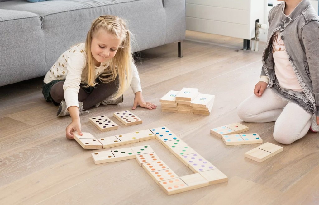 girls sitting on wood floor playing with giant wood dominos