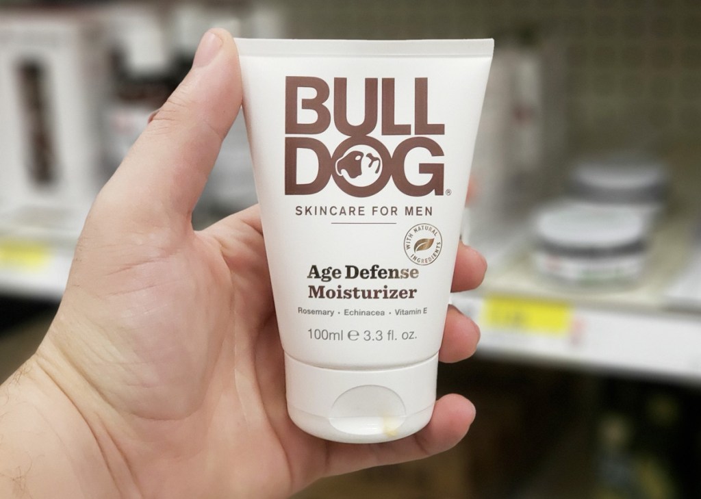 person holding up a white bottle of bulldog age defense facial moisturizer