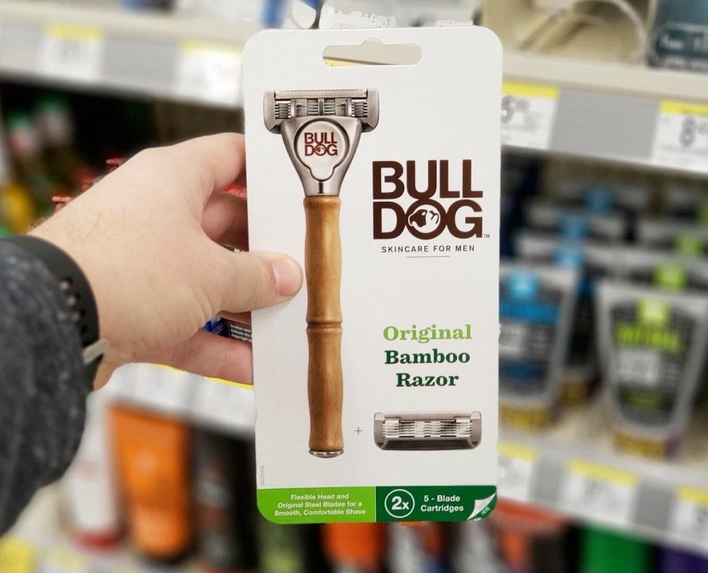 person holding up a white package of a bulldog men's razor in front of razor shelf in store