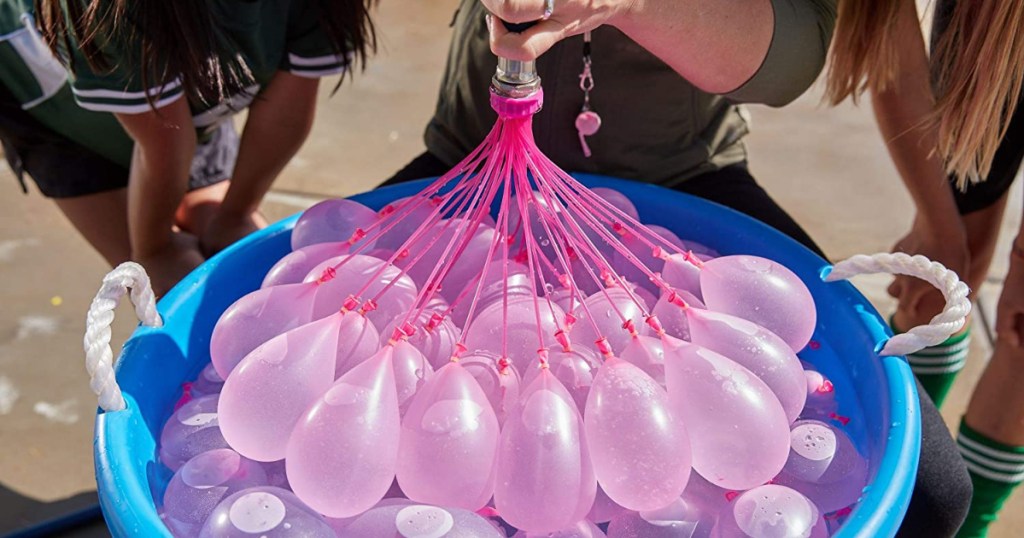 three people around tub of pink water-filled balloons