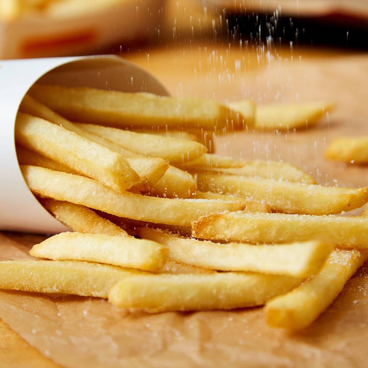 fries spilled out onto wooden counter with sea salt being sprinkled on them