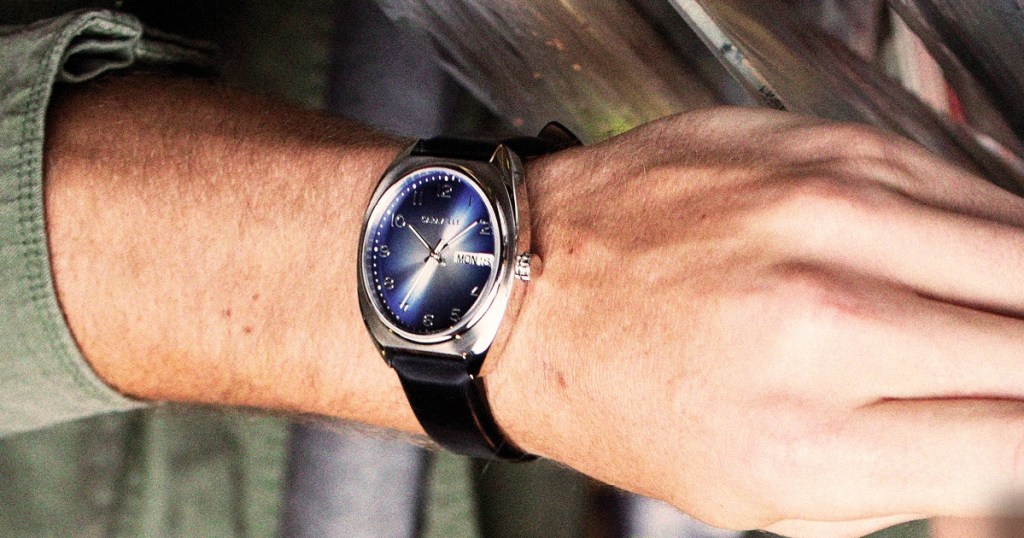man wearing a silver watch with black leather strap and blue watch face