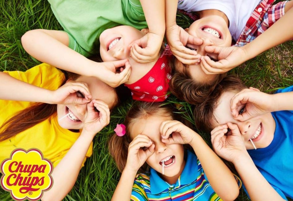 children laying in the grass on their backs holding their hand to their eyes with suckers in their mouth