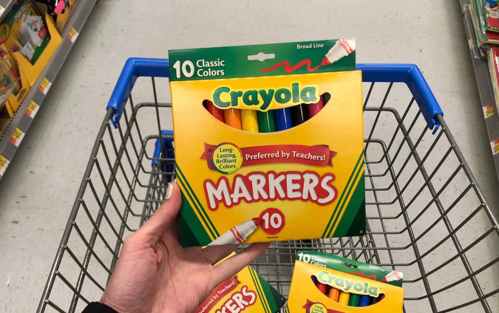 hand holding a pack of crayola markerts with more markers in walmart cart