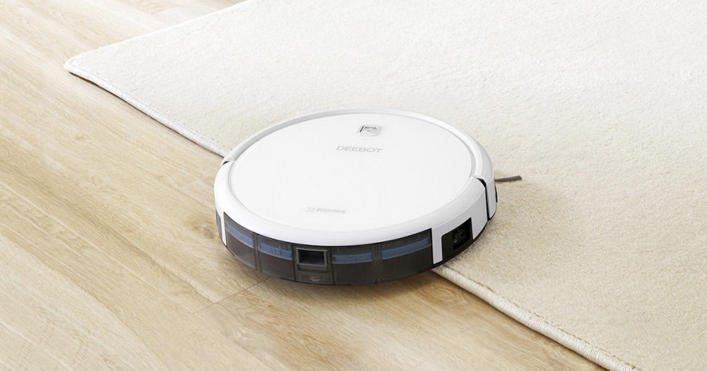 white robotic vacuum on hardwood floor moving onto a cream colored area rug