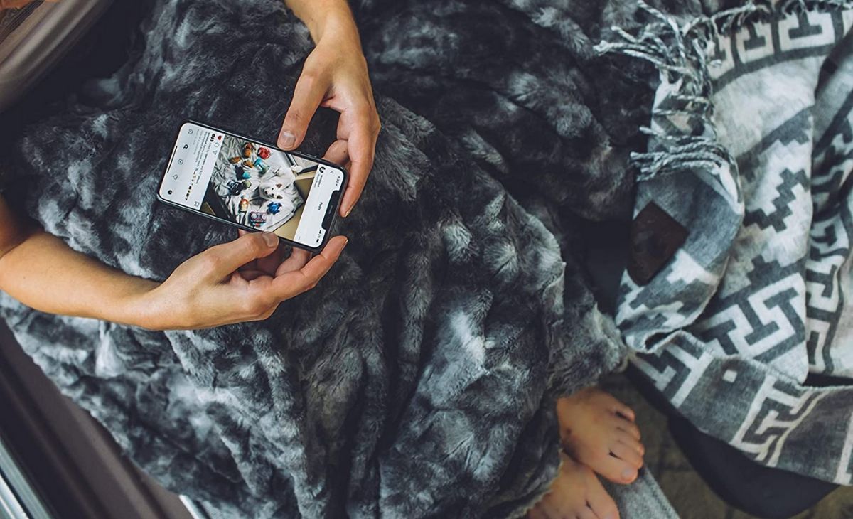 Person covered in a grey faux fur blanket and holding a phone
