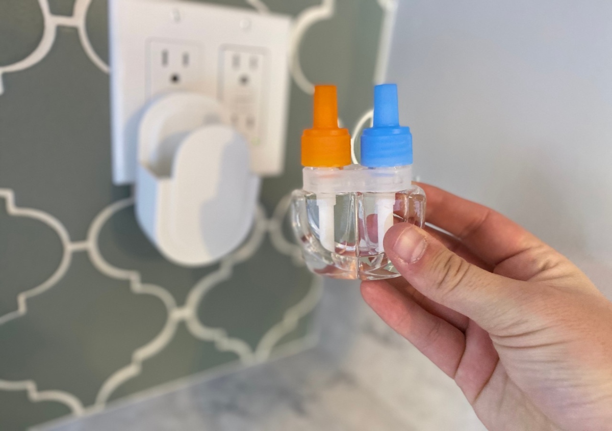 hand holding a Febreze Plug In two pack, with the plug, plugged into the outlet in the background