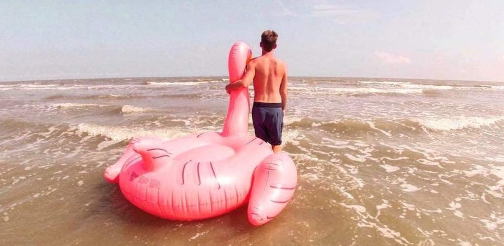 man holding onto a flamingo pool float