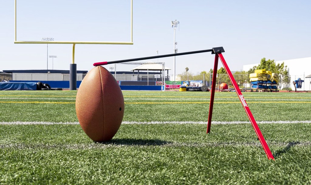 black and red football kicking tee holding football on field