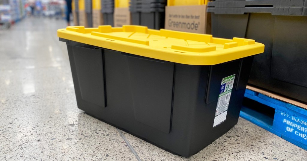 black plastic storage tote with yellow lid sitting on store floor next to display of more storage totes