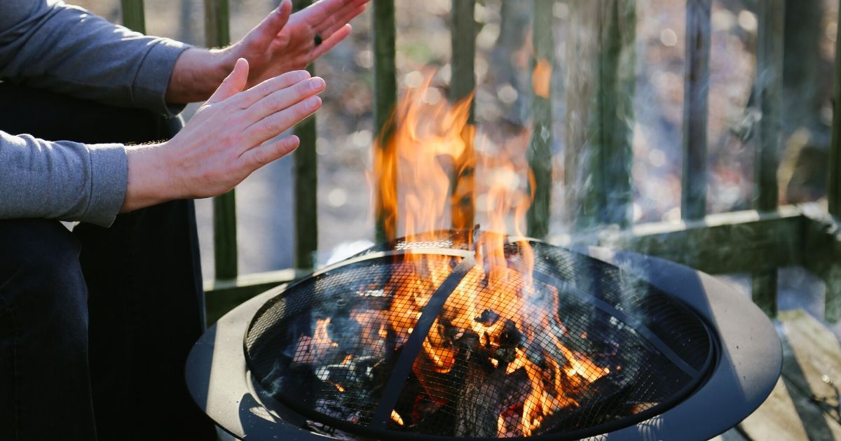 A person warming hands over a fire pit outside