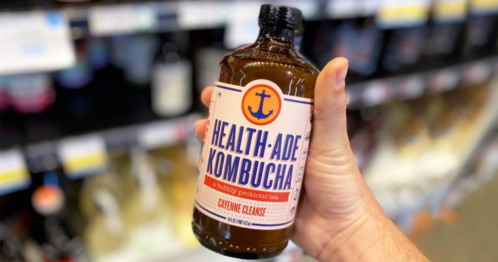 person's hand holding up a glass bottle of Health-Ade Kombucha