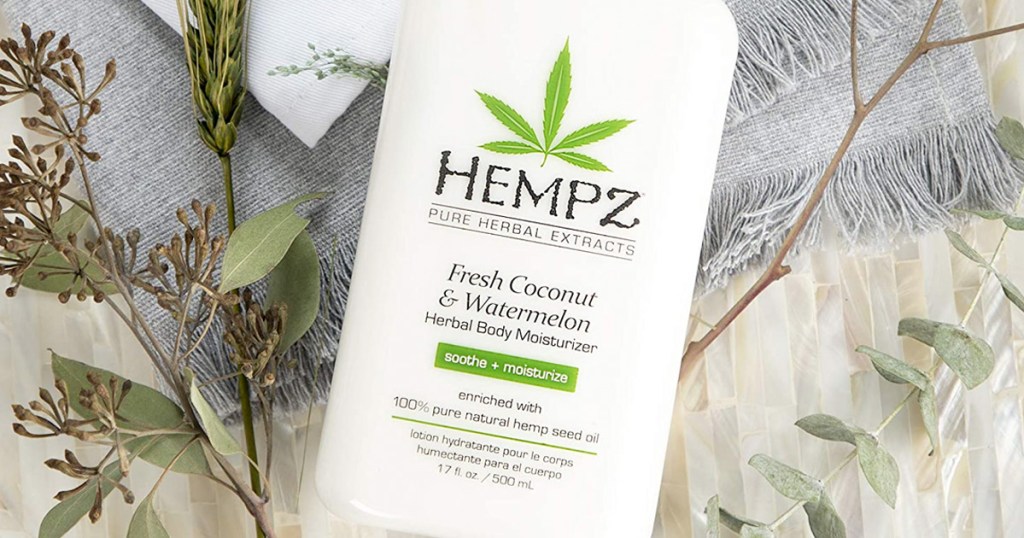 white bottle of Hempz coconut watermelon lotion laying on blanket with leaves around it
