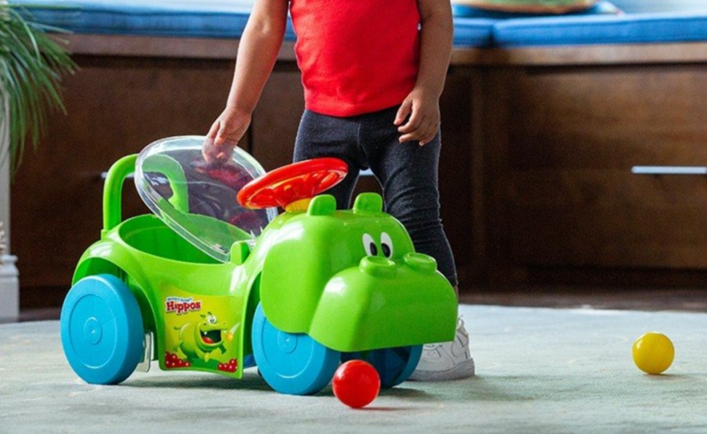 young boy standing next to hippo ride on toy in home