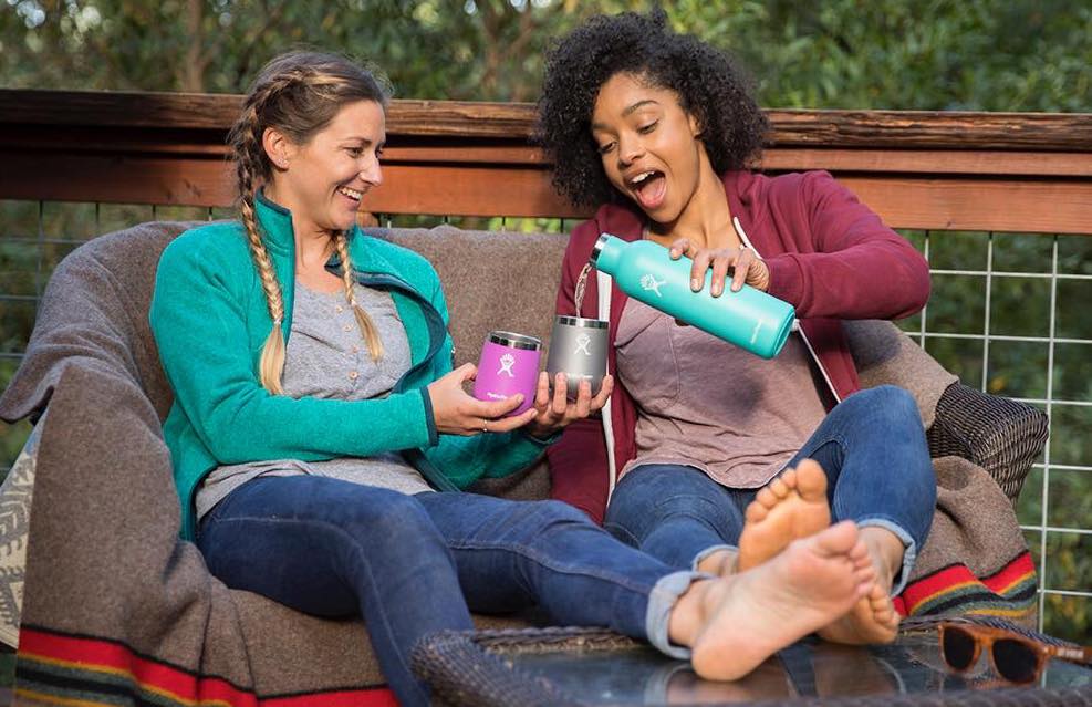 two people sitting outside while one pours the other a drink