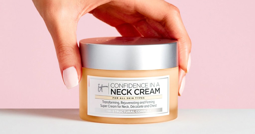 person with light pink nails holding a jar of it cosmetics neck cream on a white surface