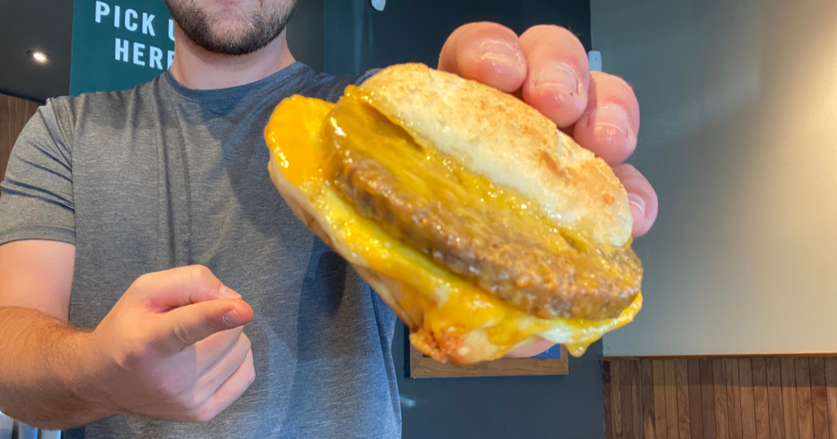 man holding sausage egg and cheese sandwich with one hand and pointing at it with other hand