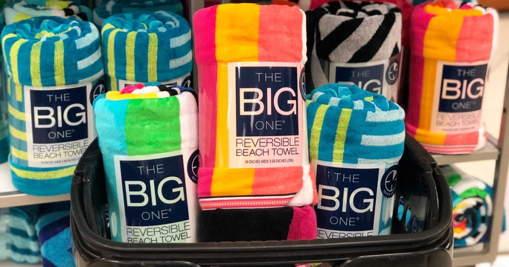black shopping basket with three rolled up beach towels in front of display of beach towels in various prints and colors