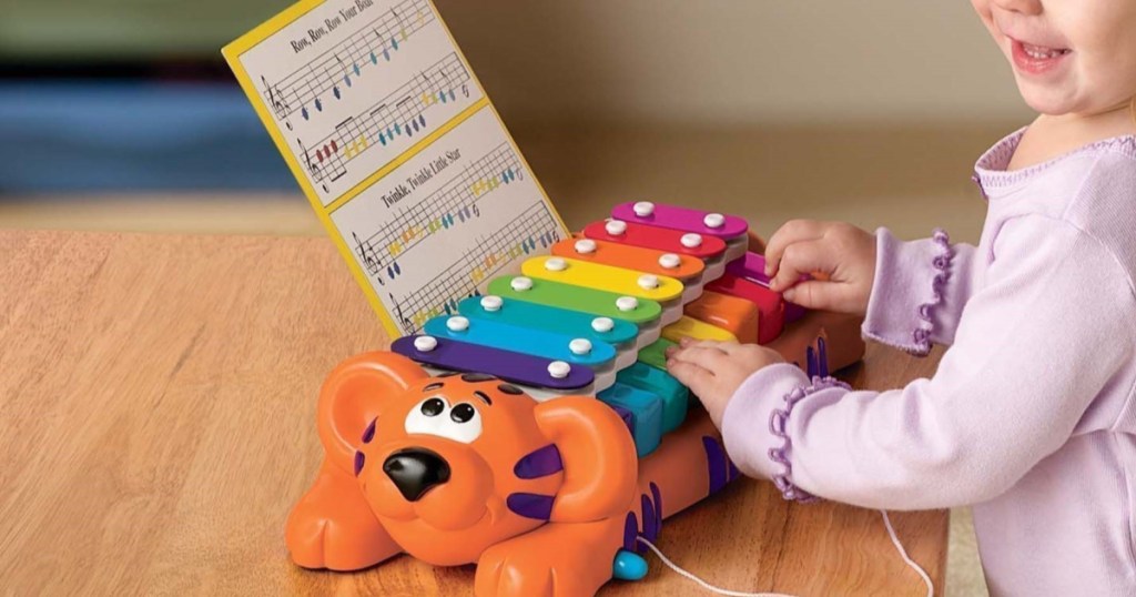 little girl playing on toy piano/xylophone on table