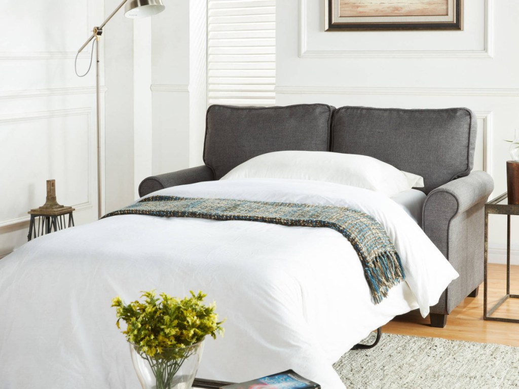 Grey Loveseat Sleeper Sofa made into a twin size bed next to a side table and plant